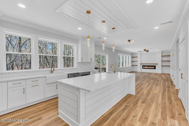 kitchen with white cabinetry, ornamental molding, a sink, and a glass covered fireplace