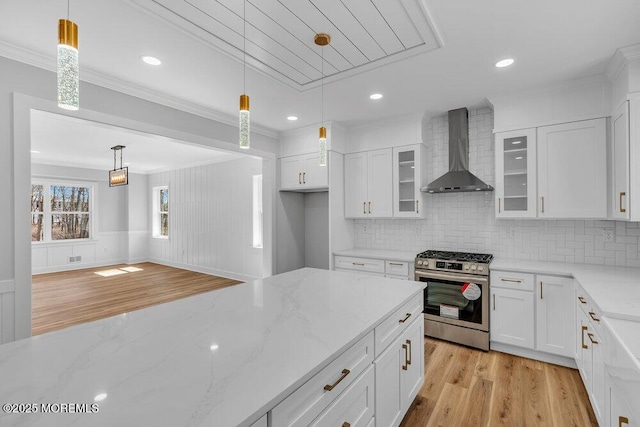 kitchen featuring light wood finished floors, stainless steel gas range oven, glass insert cabinets, crown molding, and wall chimney range hood