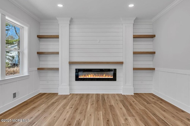 unfurnished living room featuring ornamental molding, wood finished floors, a glass covered fireplace, and visible vents