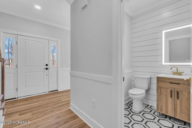 foyer with ornamental molding, wainscoting, and light wood-style flooring