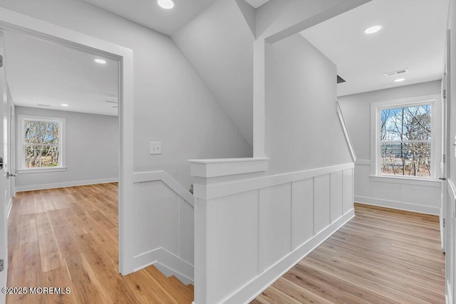 hall featuring light wood-style flooring, a wealth of natural light, and an upstairs landing