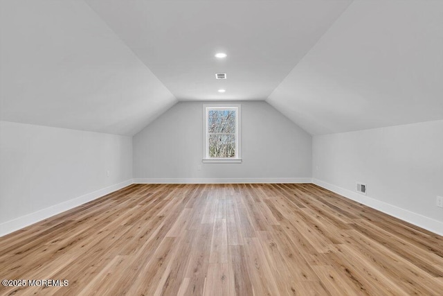 additional living space featuring light wood-type flooring, visible vents, baseboards, and lofted ceiling