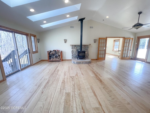 unfurnished living room with lofted ceiling with skylight, a wood stove, visible vents, and light wood-type flooring