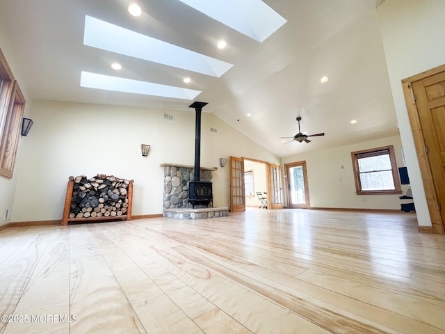 unfurnished living room featuring visible vents, high vaulted ceiling, a skylight, light wood finished floors, and a wood stove