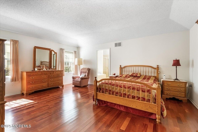 bedroom with a textured ceiling, wood finished floors, visible vents, and baseboards