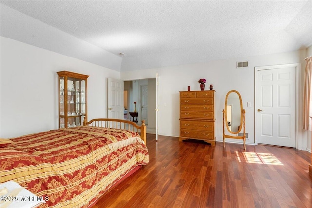 bedroom featuring baseboards, a textured ceiling, visible vents, and wood finished floors