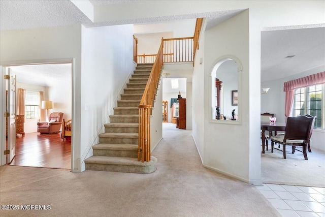 stairway with carpet floors, a towering ceiling, a textured ceiling, tile patterned flooring, and baseboards