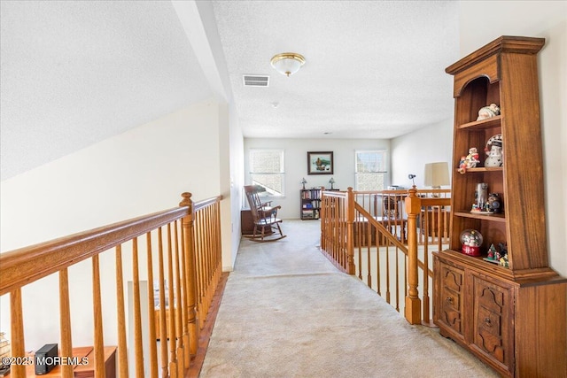 hallway featuring visible vents, light colored carpet, a textured ceiling, and an upstairs landing