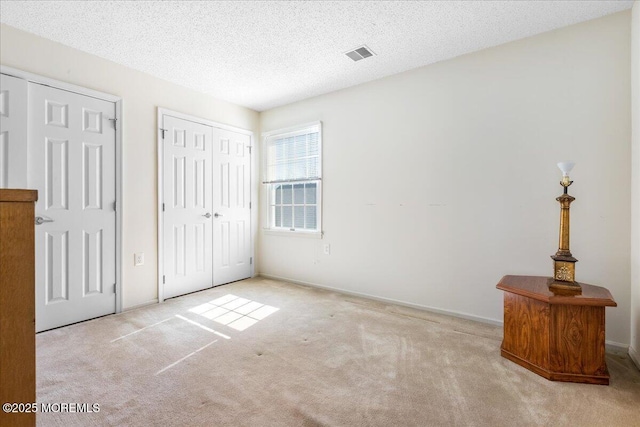 unfurnished bedroom featuring a textured ceiling, carpet floors, and visible vents