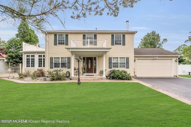 view of front of house featuring aphalt driveway, an attached garage, a balcony, fence, and a front yard