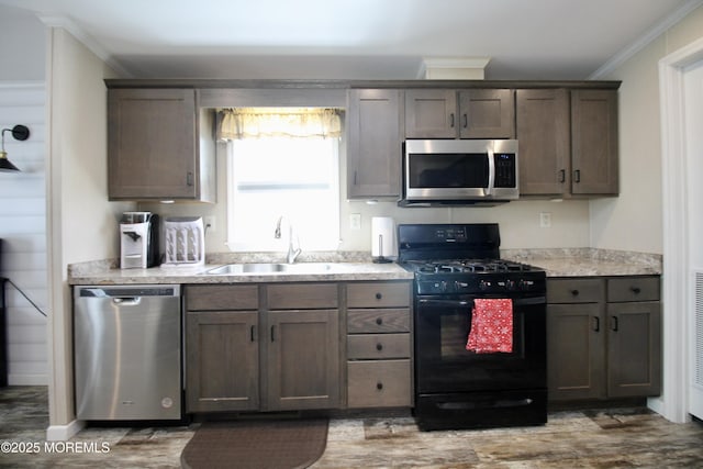 kitchen with ornamental molding, a sink, wood finished floors, appliances with stainless steel finishes, and light countertops