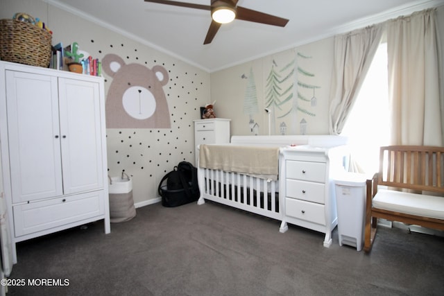 carpeted bedroom with a ceiling fan, baseboards, wallpapered walls, ornamental molding, and a nursery area