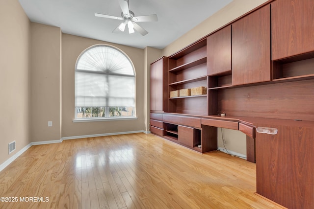 unfurnished office with visible vents, ceiling fan, baseboards, built in desk, and light wood-style floors