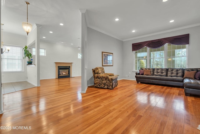 living area featuring light wood-type flooring, a glass covered fireplace, crown molding, and a chandelier