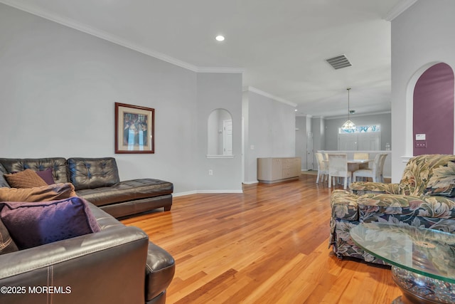 living room with light wood-type flooring, visible vents, arched walkways, and crown molding