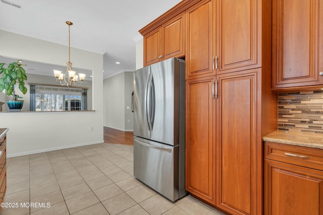 kitchen featuring light tile patterned floors, visible vents, freestanding refrigerator, decorative backsplash, and brown cabinets