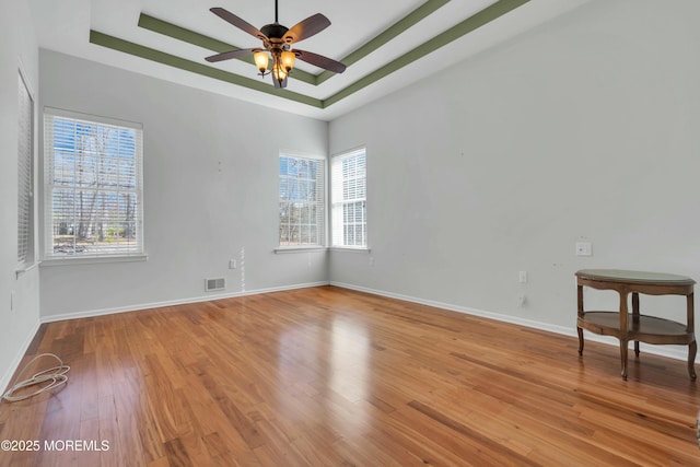 empty room with visible vents, ceiling fan, baseboards, a tray ceiling, and wood finished floors