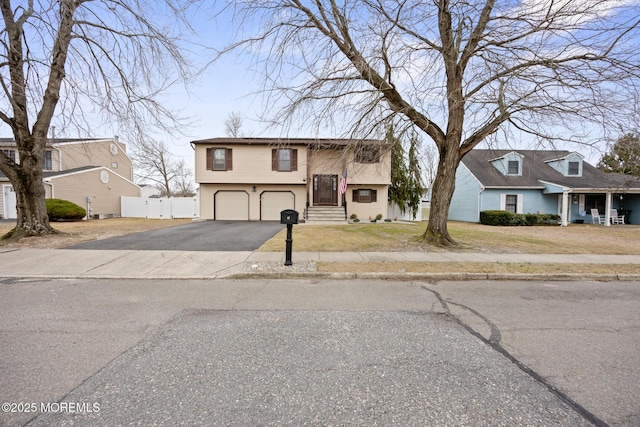 bi-level home with a garage, driveway, a front lawn, and fence