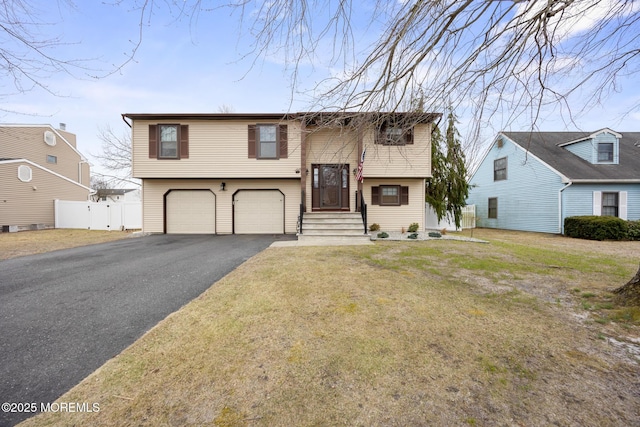 raised ranch featuring a front yard, driveway, an attached garage, and fence