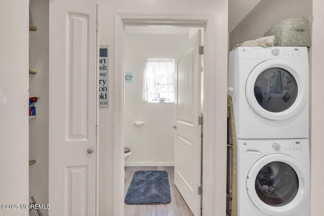 laundry area with stacked washer and clothes dryer, baseboards, and wood finished floors