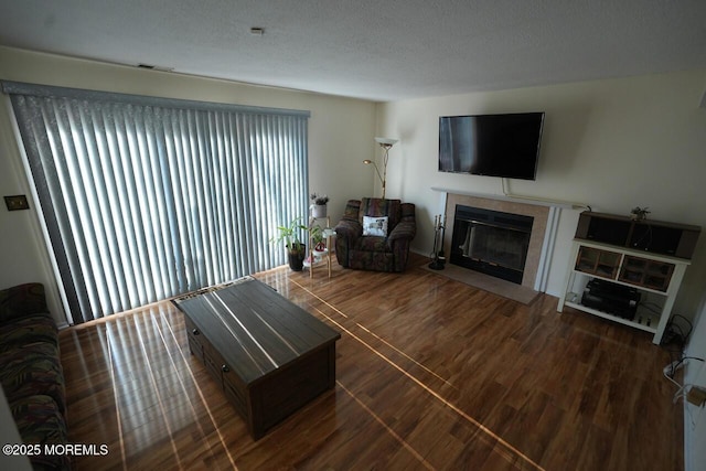 living area featuring a tile fireplace, visible vents, a textured ceiling, and wood finished floors