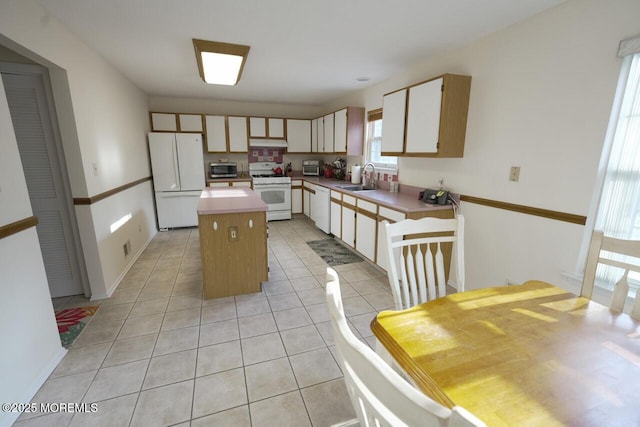 kitchen featuring white appliances, light tile patterned floors, a kitchen island, light countertops, and a sink