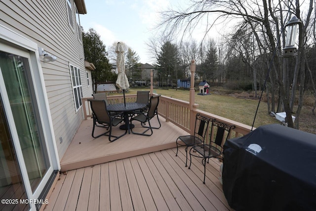 wooden deck with outdoor dining space, a lawn, and grilling area