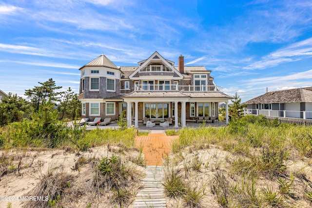 rear view of property featuring a balcony, a chimney, an outdoor hangout area, and a patio