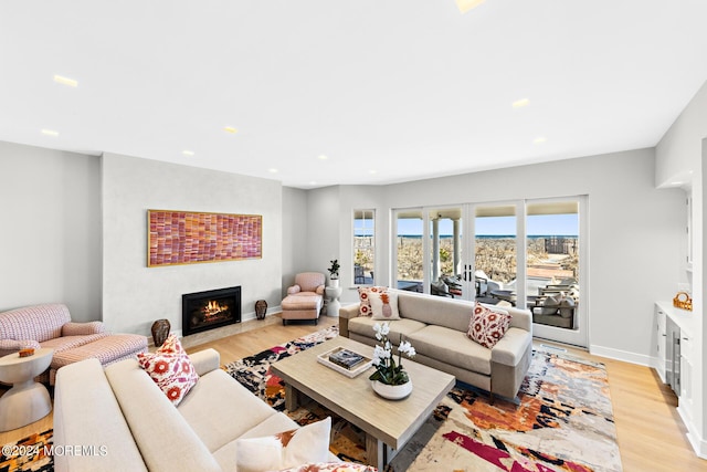 living area with french doors, light wood finished floors, recessed lighting, a warm lit fireplace, and baseboards