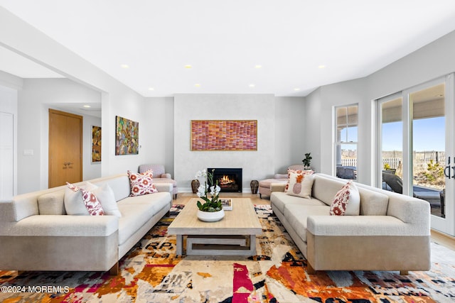 living area featuring a warm lit fireplace, baseboards, wood finished floors, and recessed lighting