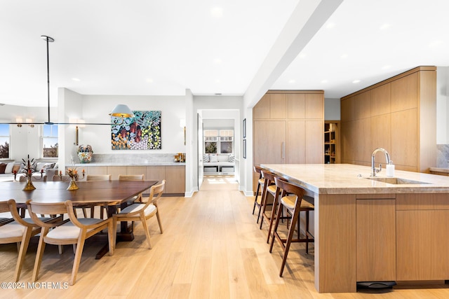 kitchen with light stone counters, a sink, a kitchen breakfast bar, light wood-type flooring, and modern cabinets