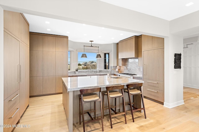 kitchen featuring light wood-style flooring, modern cabinets, light stone countertops, and decorative backsplash