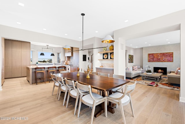 dining room featuring light wood-style floors, recessed lighting, a large fireplace, and stairs