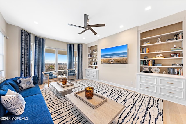 living room featuring built in shelves, recessed lighting, light wood-style flooring, ceiling fan, and baseboards