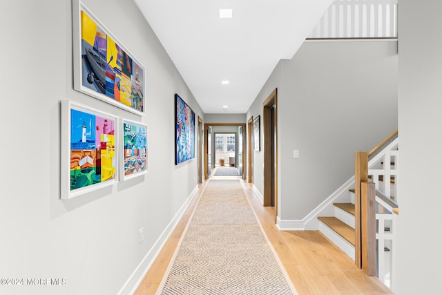 corridor with stairs, baseboards, and light wood-style floors