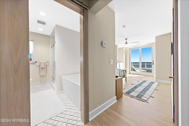 hall with light wood finished floors, a barn door, visible vents, and baseboards