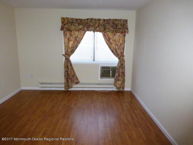 spare room featuring baseboard heating, a wall unit AC, wood finished floors, and baseboards