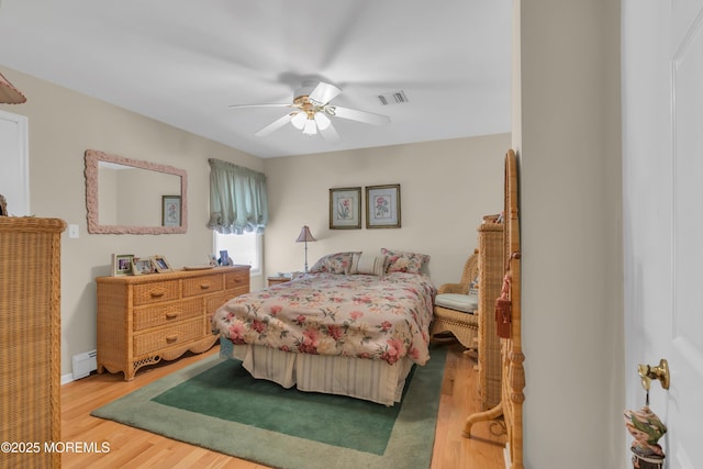 bedroom with visible vents, ceiling fan, baseboard heating, and wood finished floors