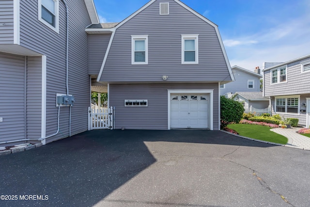 view of side of property with a garage, driveway, a gambrel roof, and fence