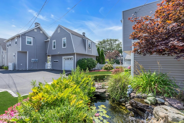 view of side of home with aphalt driveway, a garage, fence, a garden pond, and a gambrel roof