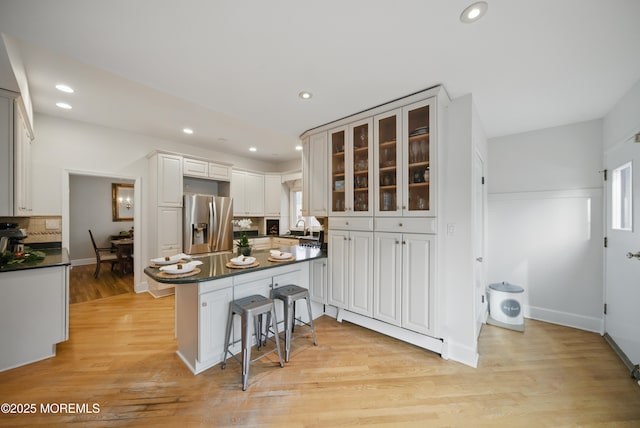 kitchen with light wood finished floors, dark countertops, a sink, and stainless steel fridge with ice dispenser