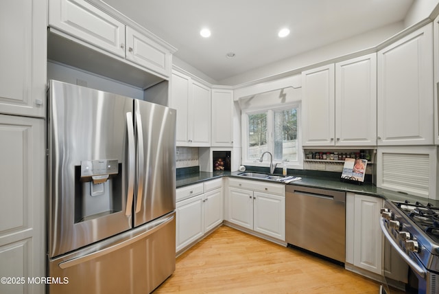 kitchen featuring stainless steel appliances, dark countertops, a sink, and white cabinetry