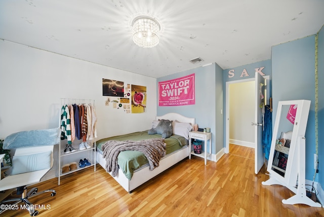 bedroom with an inviting chandelier, baseboards, visible vents, and wood finished floors