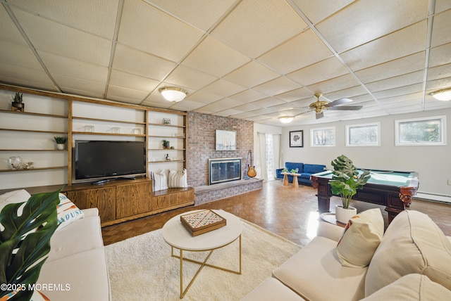 living room with a paneled ceiling, a brick fireplace, and built in shelves