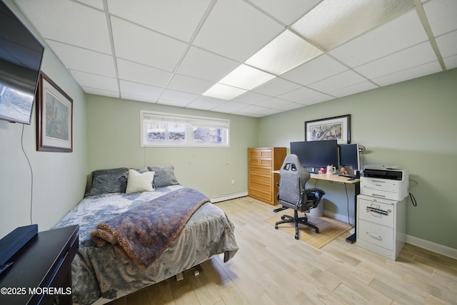 bedroom featuring light wood finished floors, baseboard heating, a drop ceiling, and baseboards