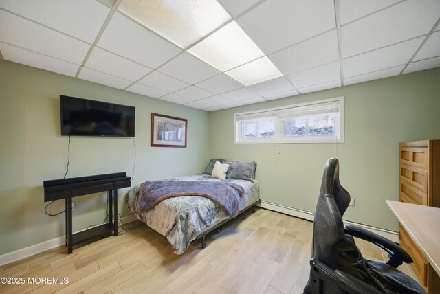 bedroom featuring light wood finished floors, a baseboard radiator, a paneled ceiling, and baseboards