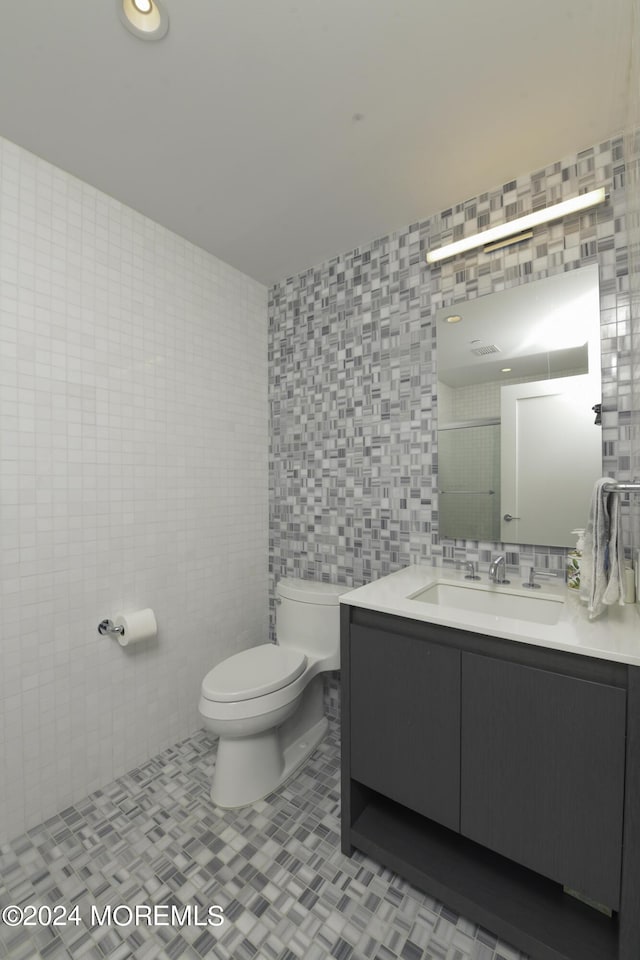 bathroom featuring tile patterned flooring, tile walls, toilet, and vanity