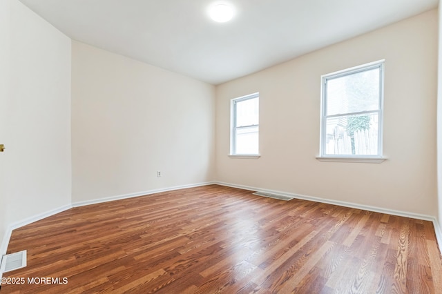 empty room with wood finished floors, visible vents, and baseboards