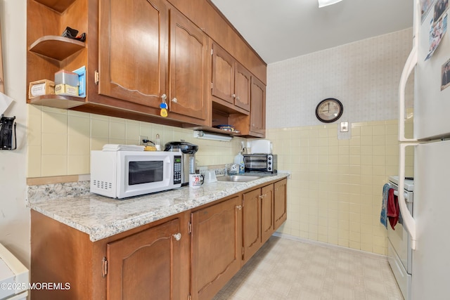 kitchen featuring light floors, open shelves, brown cabinetry, white appliances, and wallpapered walls