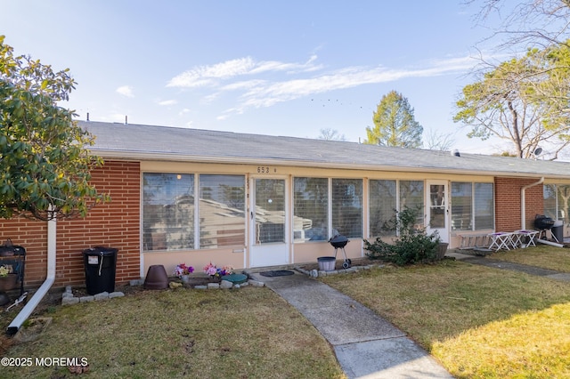 view of front of property with brick siding, a front yard, and a sunroom